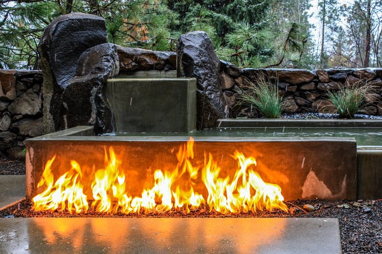Outdoor fire burner by water feature in a residential backyard
