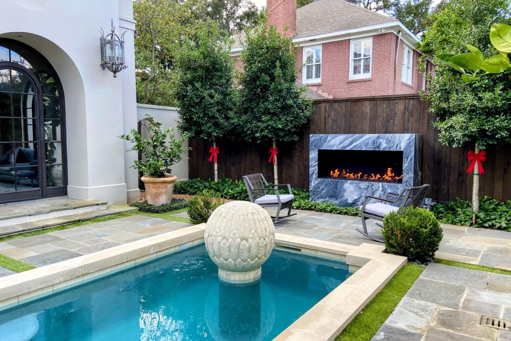 A luxurious outdoor space with a pool featuring a custom open outdoor gas fireplace with black reflective glass media.