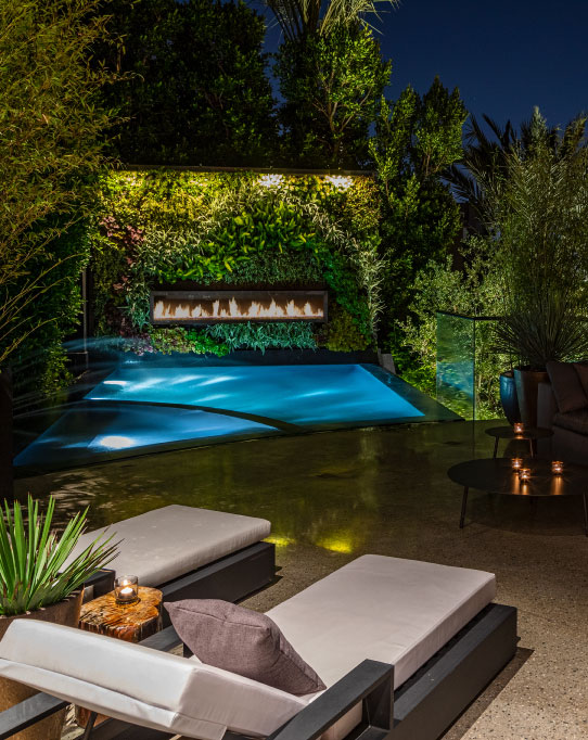 Linear fireplace in a plant wall overlooking a pool