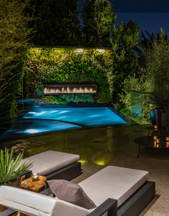 Lounge chairs overlooking a pool surrounded by greenery at night