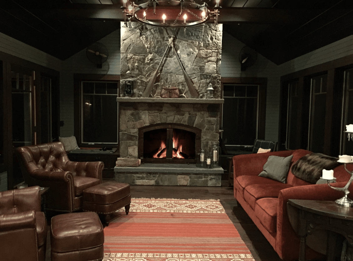 A dark living room filled with plush, dark furniture oriented around a stonework fireplace