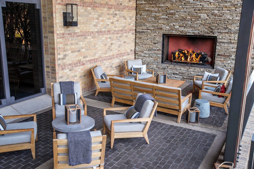 A comfortable outdoor patio featuring a single-sided open gas fireplace with a log set.