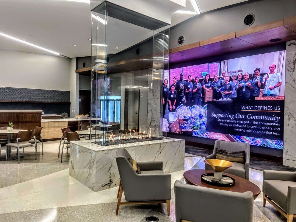 a four sided fireplace in a hotel lobby by a huge screen