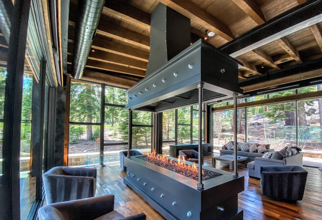 a four sided gas fireplace in the middle of a living room in a cabin