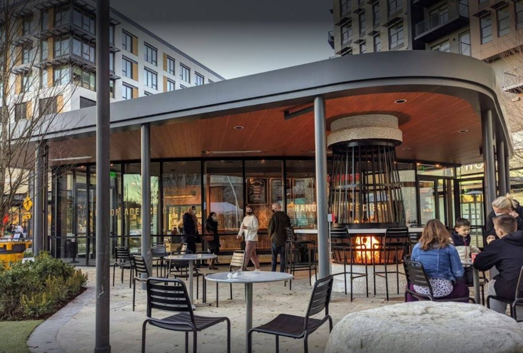 the outside of a cafe in an outdoor mall with a round outdoor fireplace