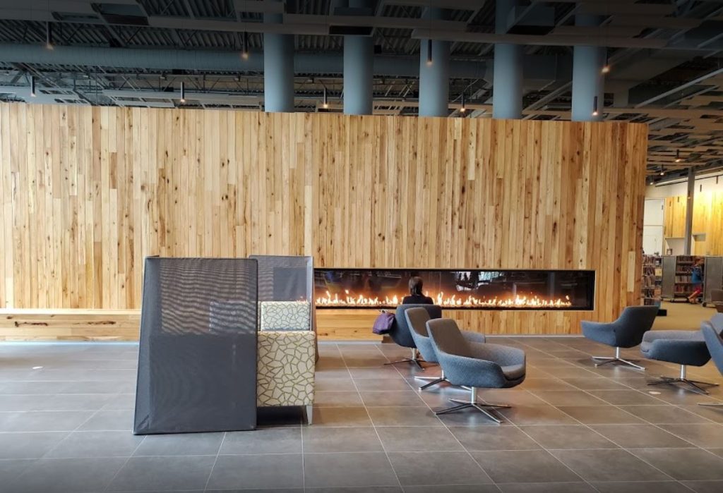 a photo of a library lounge in olathe kansas with a long linear gas fireplace with wood surround