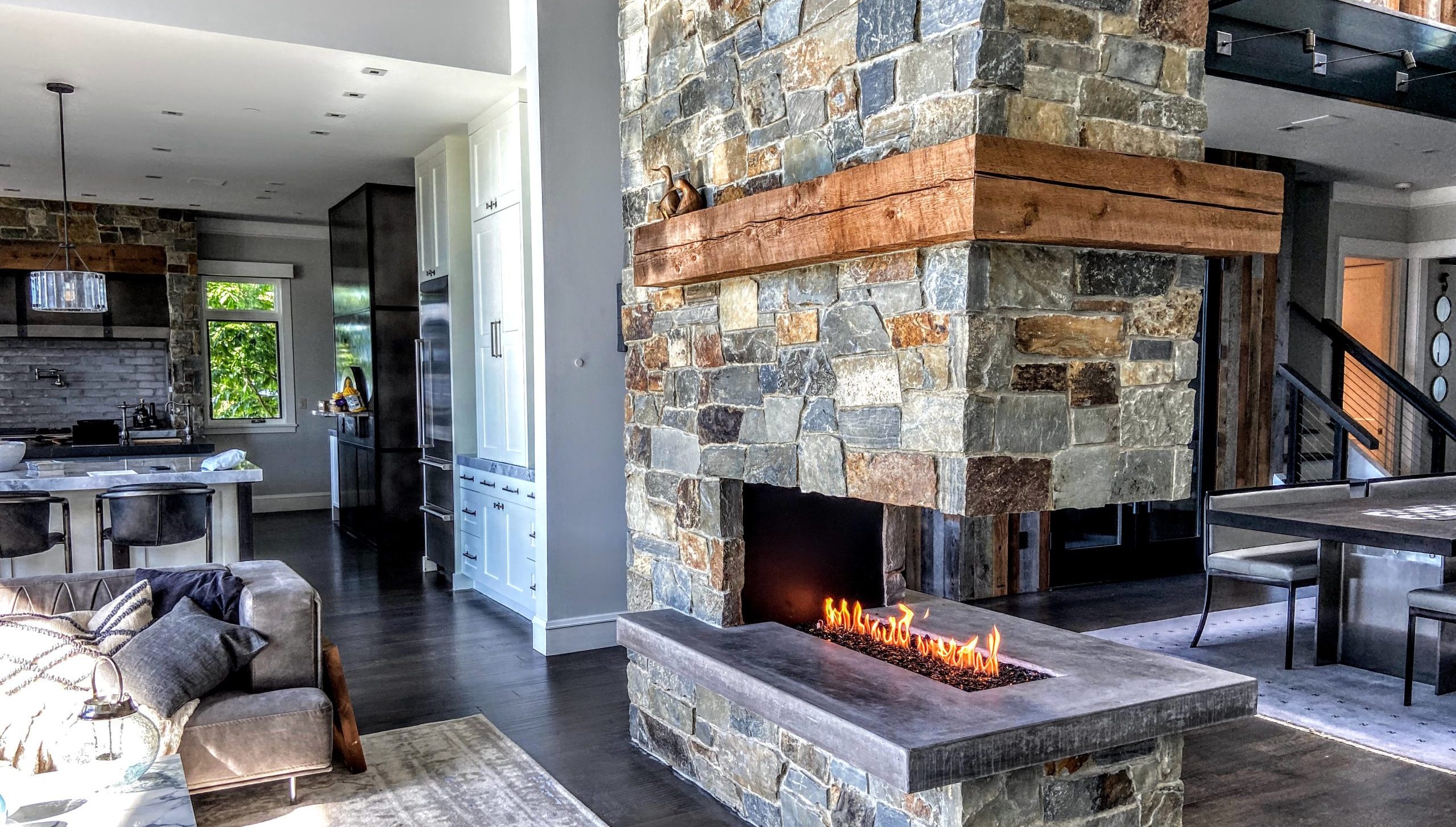 Modern living space with a custom Acucraft stone peninsula gas fireplace with a wooden mantel.