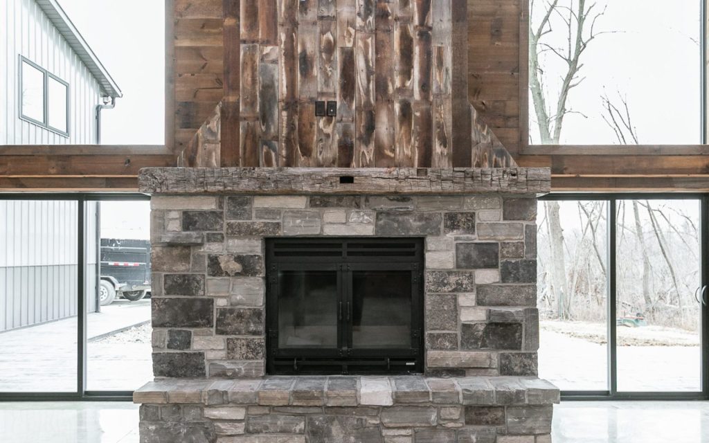 a large wood burning fireplace with stone finish in a barndominium living room