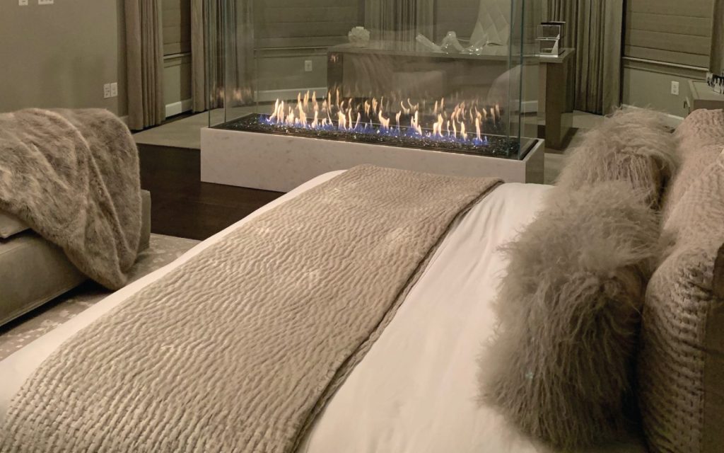 a four sided glass fireplace in a cozy master bedroom with office