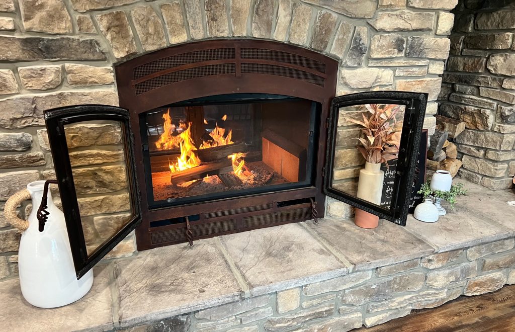 A standard wood-burning fireplace with its doors open, creating a warm, open-hearth ambiance in a traditional living room.