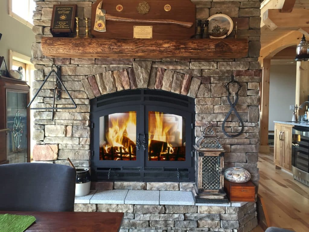 A double-sided wood-burning fireplace serving as a warm divider between a living room and dining area, framed by elegant natural wood finishes