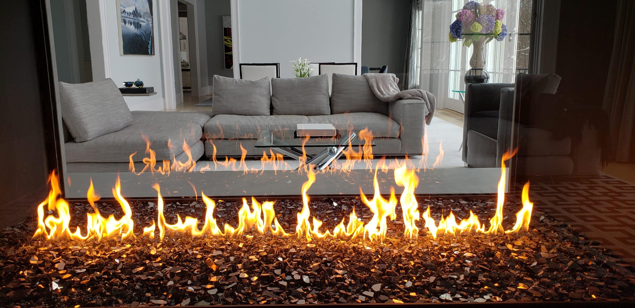 Modern living room with a custom linear see-through natural gas fireplace, black reflective glass media, and matte black frame.