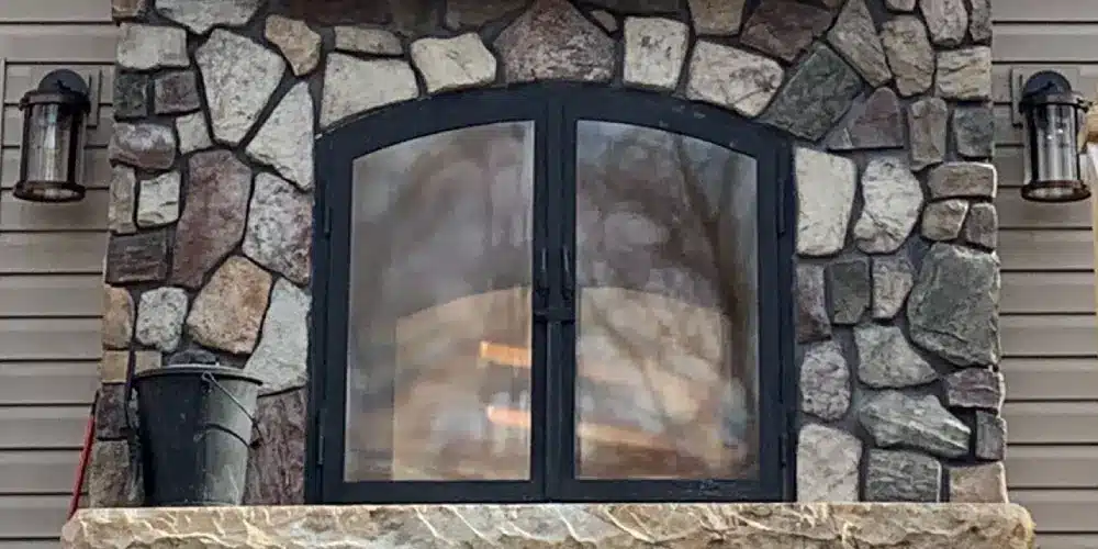an image of an indoor outdoor wood burning fireplace with stone masonry chimney