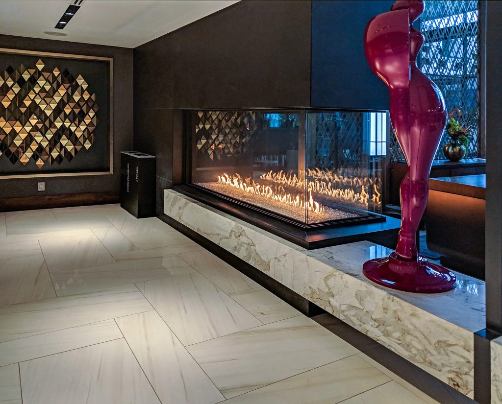 A three-sided gas fireplace used as a stylish room divider, creating a warm and inviting atmosphere in a shared living area.