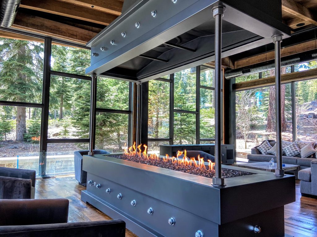 Industrial-style open-view gas fireplace by Acucraft in a luxury mountain retreat with panoramic forest views