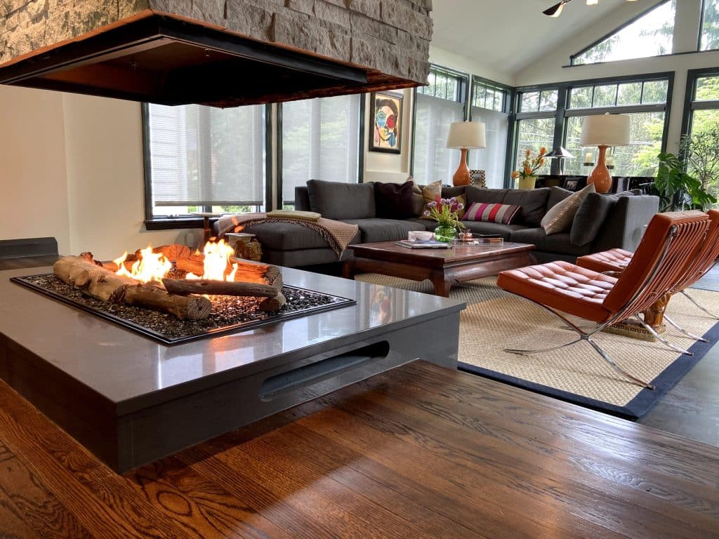 Modern living room with a custom open-view gas fireplace by Acucraft featuring realistic log media and stone surround