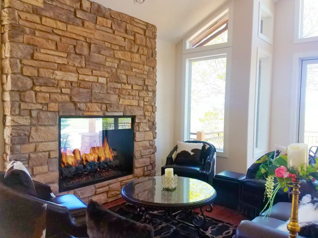 Acucraft custom gas indoor-outdoor fireplace set in a stone wall in a bright living space