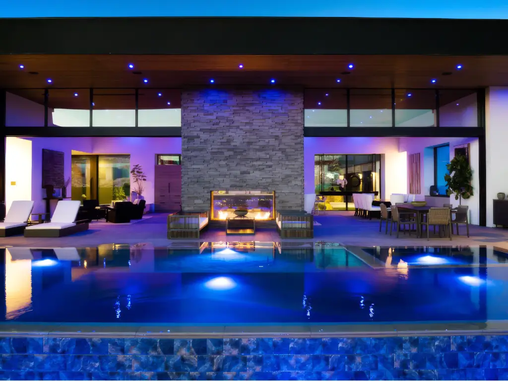 Acucraft custom indoor-outdoor gas fireplace centered between a luxury pool and covered living area