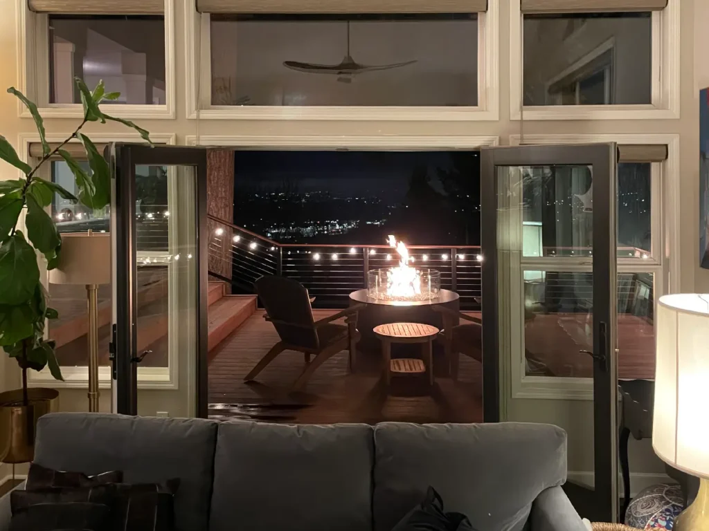Acucraft custom circular gas fire table on a deck viewed through open patio doors at night