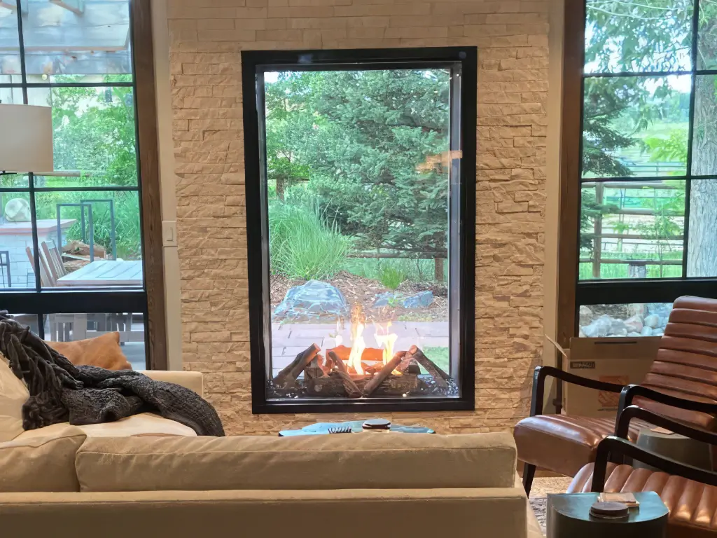 Tall Acucraft see-through gas fireplace framing an outdoor view from a living room