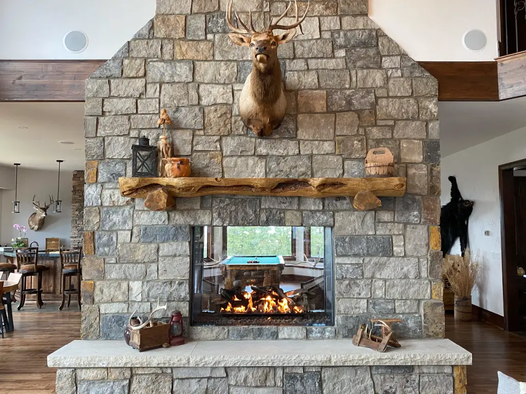 Acucraft custom see-through gas fireplace in a large stone wall connecting two rooms