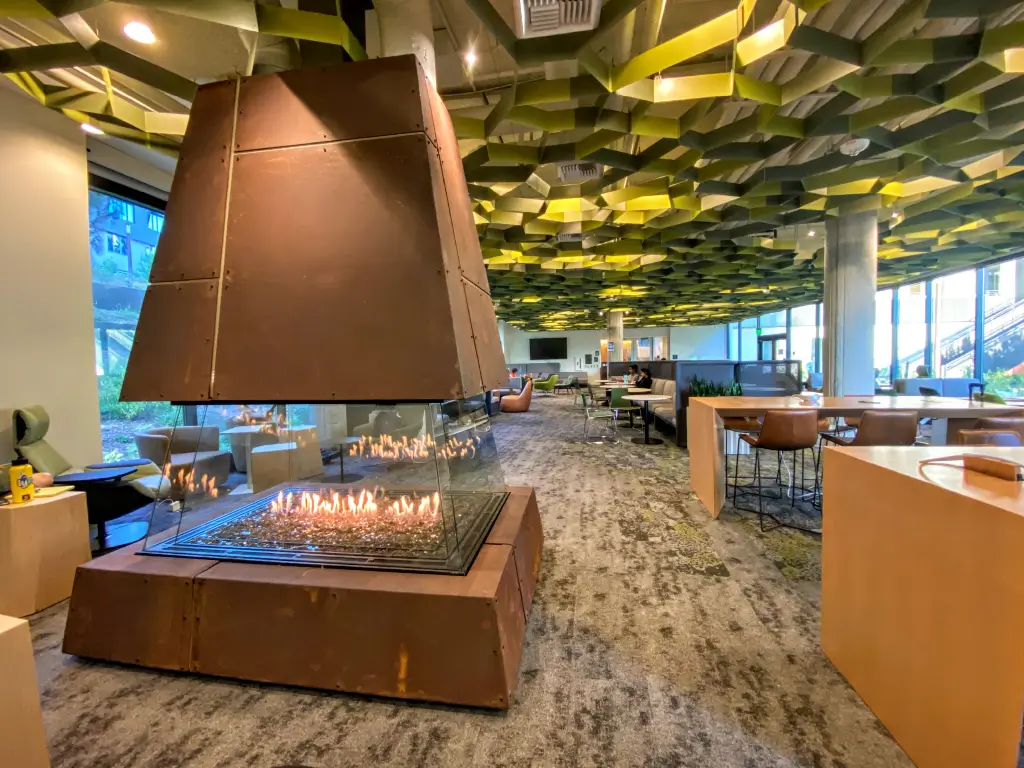Acucraft four-sided gas fireplace with a sculptural copper hood in an open gathering space.