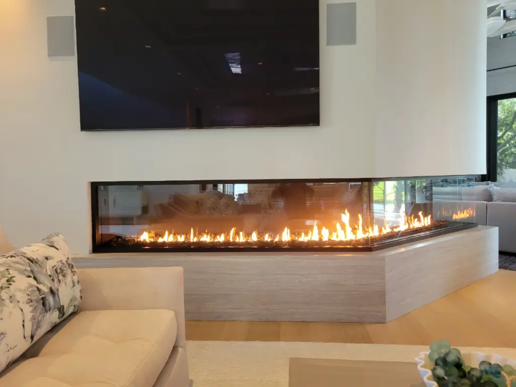 Acucraft custom front-and-side gas fireplace wrapping around a corner beneath a television.