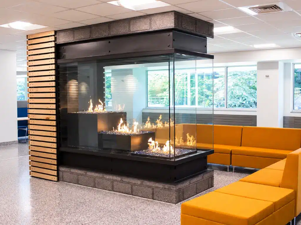 Acucraft custom gas peninsula fireplace with stepped flame levels beside yellow lounge seating.