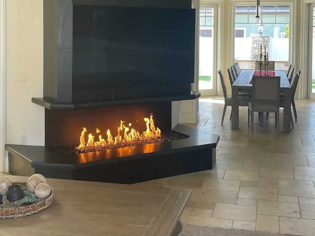 Acucraft open panoramic gas fireplace connecting a living room with an adjoining dining area.