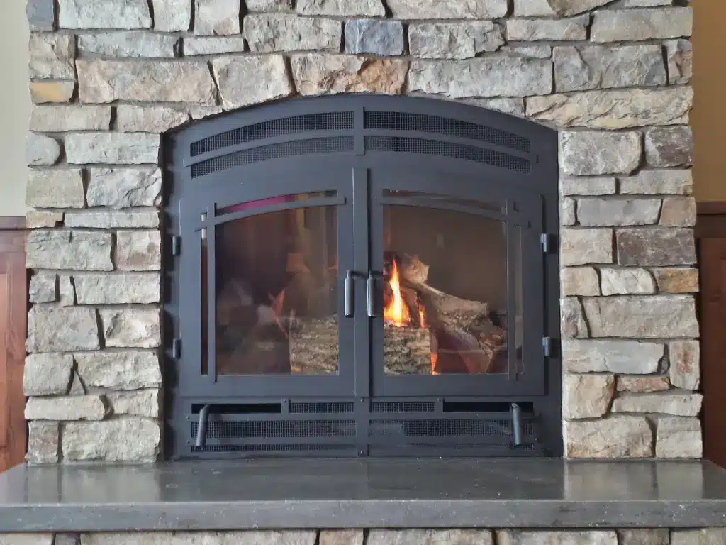 Acucraft Hearthroom 36 single-sided wood fireplace with arched glass doors in a stone surround.