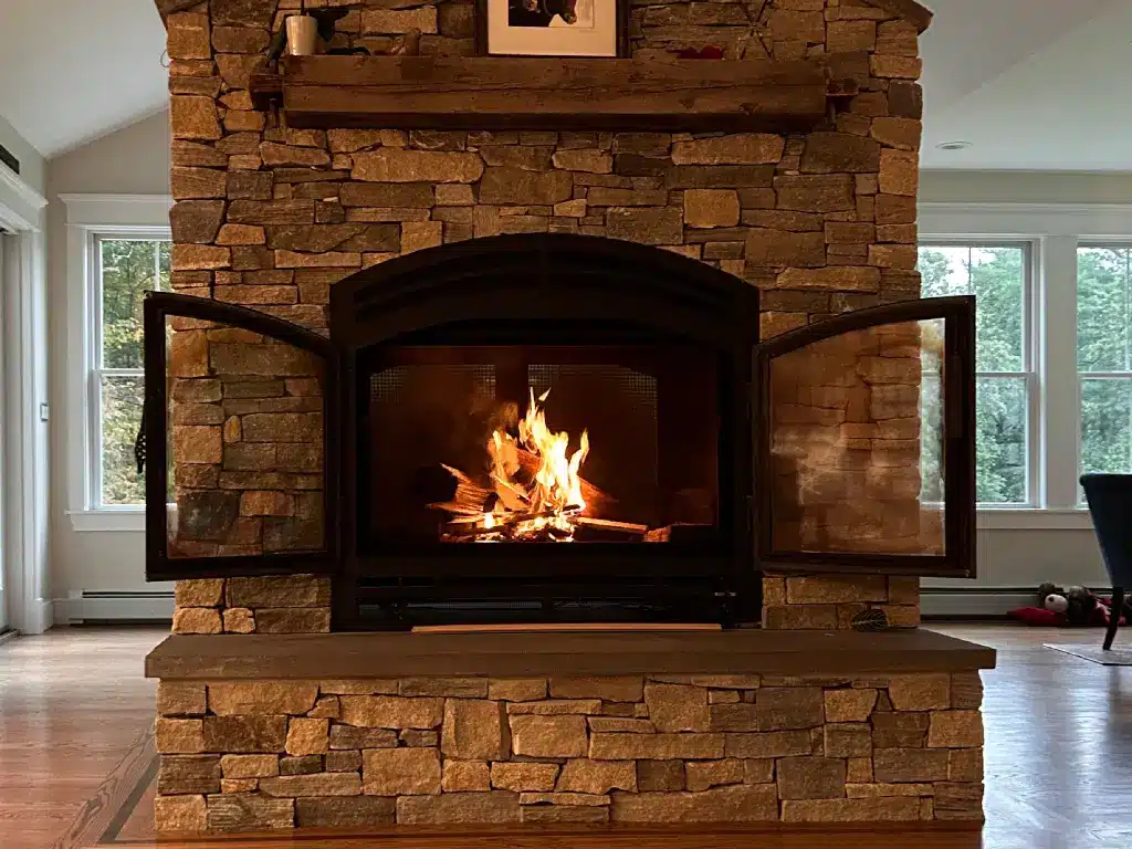Acucraft Hearthroom 44 see-through wood-burning fireplace with both doors open in a stone feature wall.