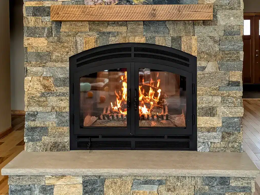 Acucraft Hearthroom 44 see-through wood-burning fireplace set beneath a wood mantel in a stone wall.
