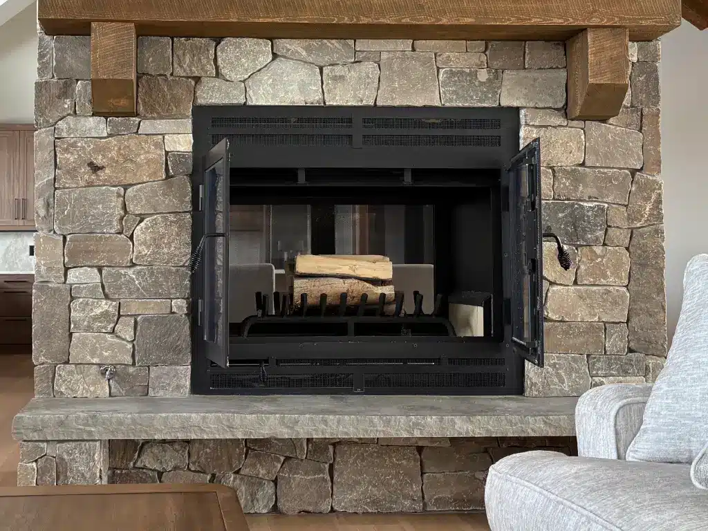 Acucraft Hearthroom 44 see-through wood fireplace with open doors and stacked logs in a stone surround.