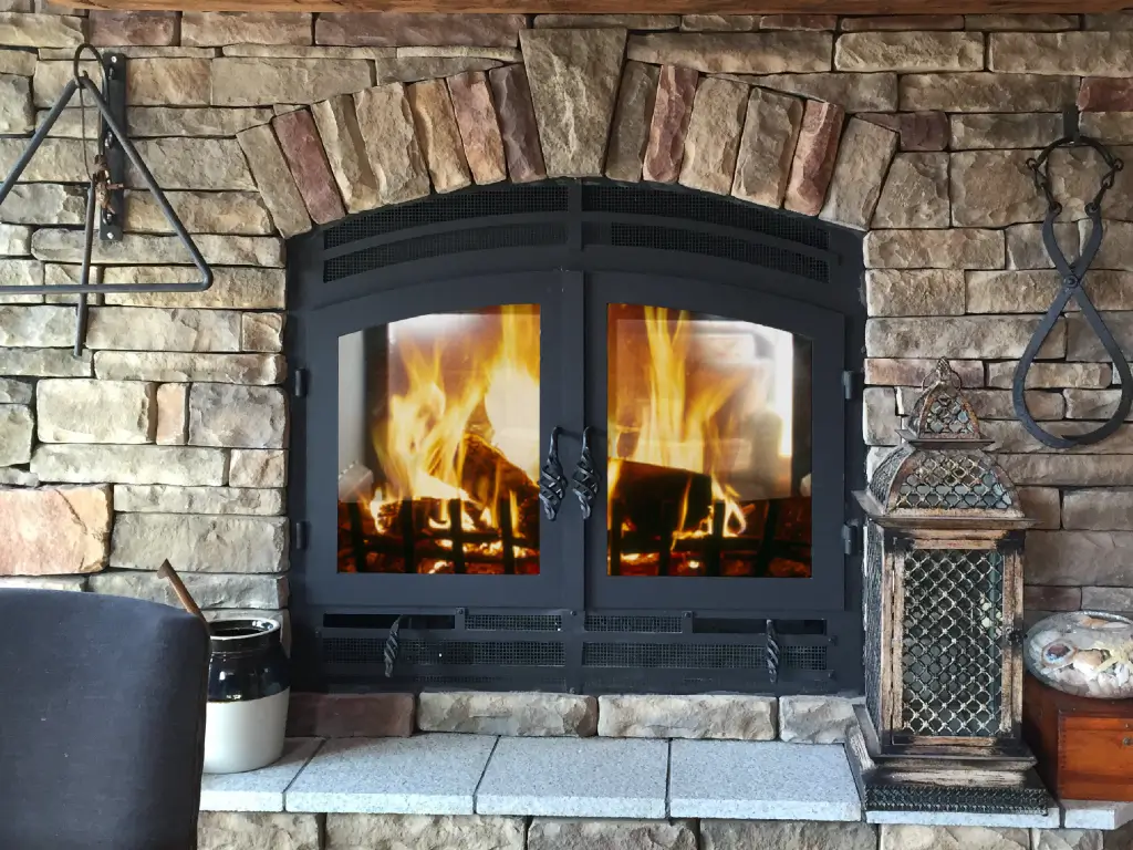 Acucraft Hearthroom 44 see-through wood fireplace with closed glass doors and fireplace tools beside the hearth.